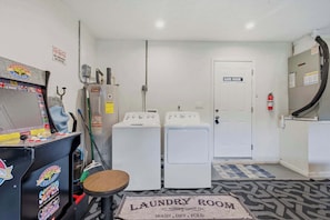 Un cuarto de lavandería con dos lavadoras, una secadora y una puerta que lleva a la sala de juegos.