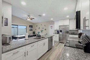 Una cocina moderna con armarios blancos, encimeras de granito, electrodomésticos de acero inoxidable y un ventilador de techo.