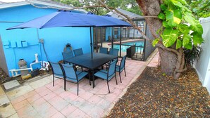 Un patio con una mesa y sillas, una sombrilla azul y una piscina al fondo.