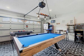 A pool table in a room with a garage door, a refrigerator, and arcade games.