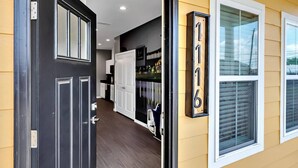 Una entrada moderna con una puerta negra, un muro exterior amarillo y un letrero con el número 1116.