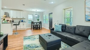 A modern living room with a black sofa, a dining area with a table and chairs, and a kitchen with white cabinets. - Elegant Atlanta Haven | 3 Bedroom Near Downtown (Atlanta)