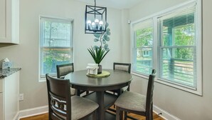 A dining area with a round table, four chairs, a hanging light fixture, and two windows with blinds. - Elegant Atlanta Haven | 3 Bedroom Near Downtown (Atlanta)