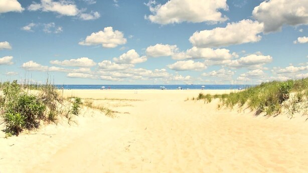 A sandy beach with dunes and a clear blue sky.