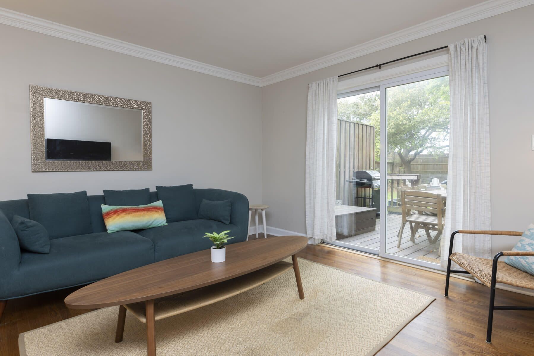 Ein Wohnzimmer mit einem dunkelgrünen Sofa, einem Holztisch und einer kleinen Pflanze. Ein Schiebetürenfenster führt auf eine Außenpatio-Terrasse mit Tisch und Stühlen.