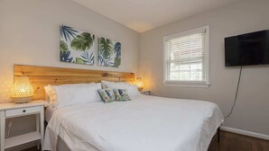 A neatly made bed with white bedding, two bedside lamps, and a wall-mounted TV.