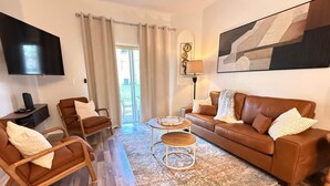 A modern living room with a brown leather sofa, two armchairs, a coffee table, and a TV mounted on the wall.