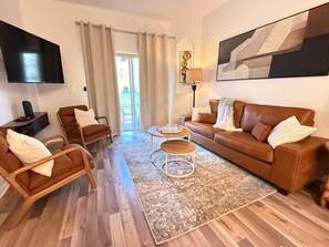 Una sala de estar moderna con un sofá de cuero marrón, dos sillones, una mesa de centro y un televisor montado en la pared.