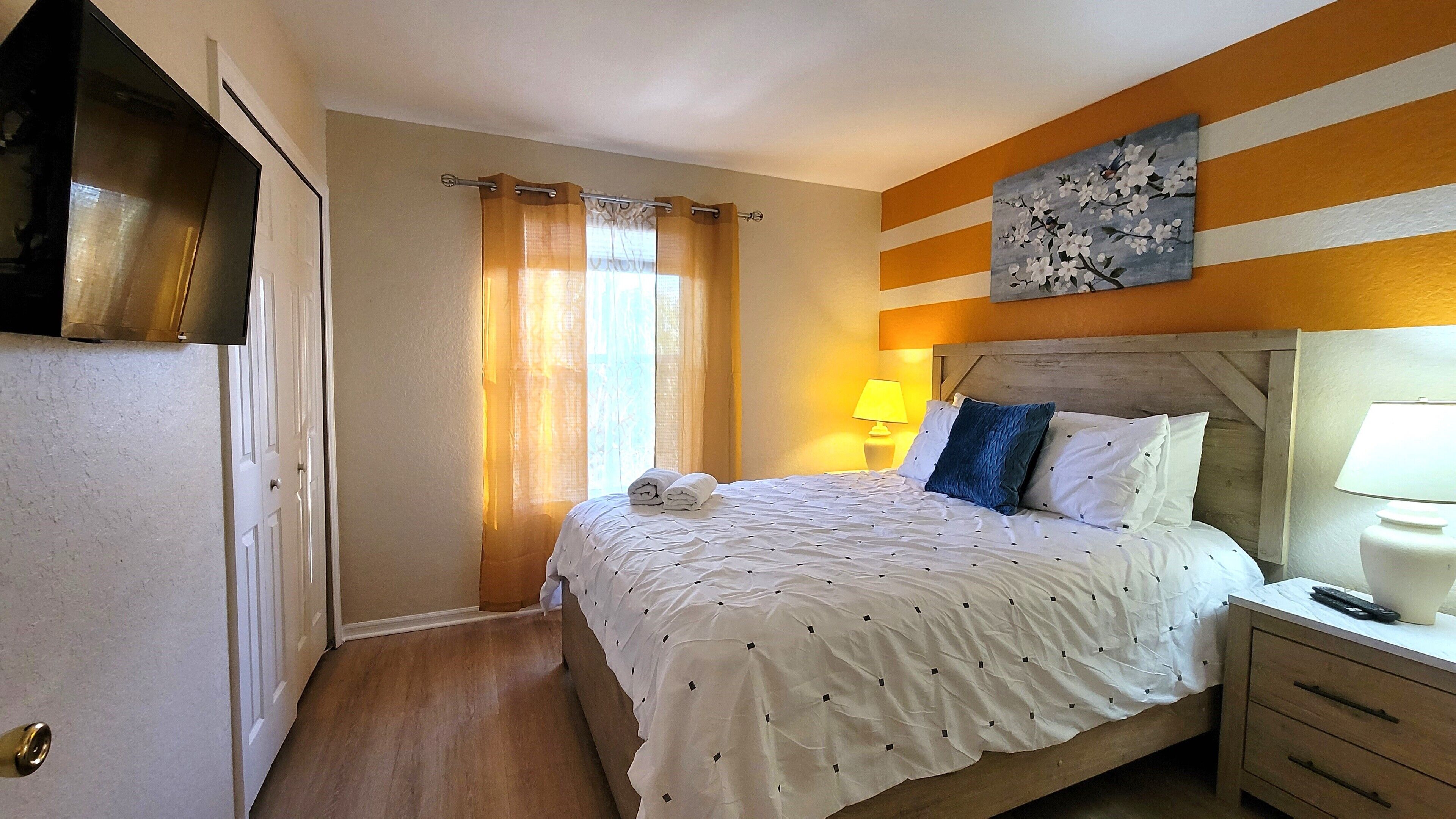 A hotel room with a bed, a nightstand, a lamp, a painting, and a door.