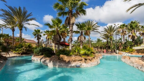A pool area with clear blue water, surrounded by palm trees and rocks.