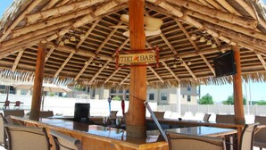 A tiki bar with a thatched roof, wooden tables, and chairs.