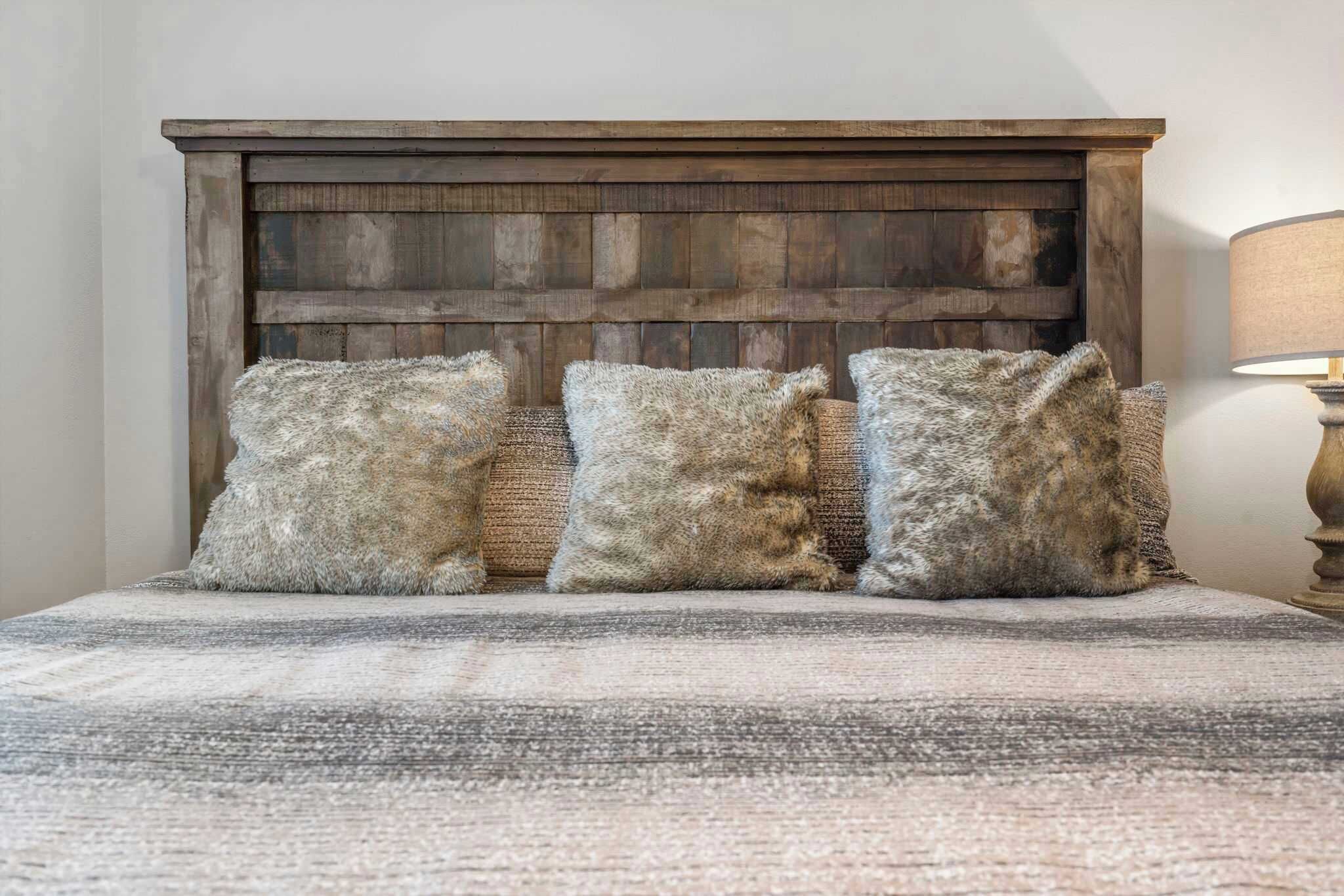 A bed with a wooden headboard and three fluffy pillows.