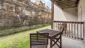 A patio with a wooden table and chairs, a stone wall, and a building in the background. - The Moab - Swimming Pool! (Branson)