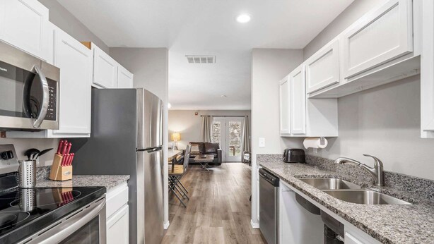 A modern kitchen with white cabinets, stainless steel appliances, granite countertops, and a central island with seating. - The Moab - Swimming Pool! (Branson)