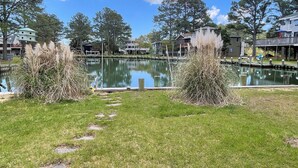 A serene lakeside view with a dock, grassy areas, and residential buildings in the background.