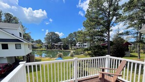 A wooden deck with a white railing, a bench, and a view of a lake with houses in the background.