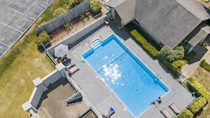 Vista aérea de una propiedad residencial con piscina rectangular, un porche cubierto y jardín cercado.