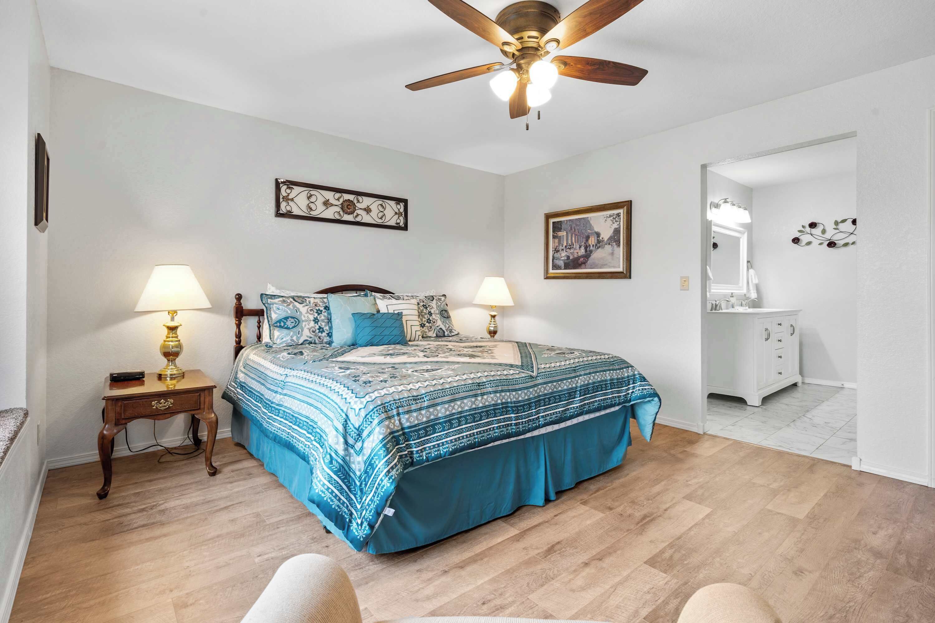 Une chambre à coucher comprenant un lit, deux tables de chevet avec des lampes, un ventilateur de plafond, une commode et un miroir.
