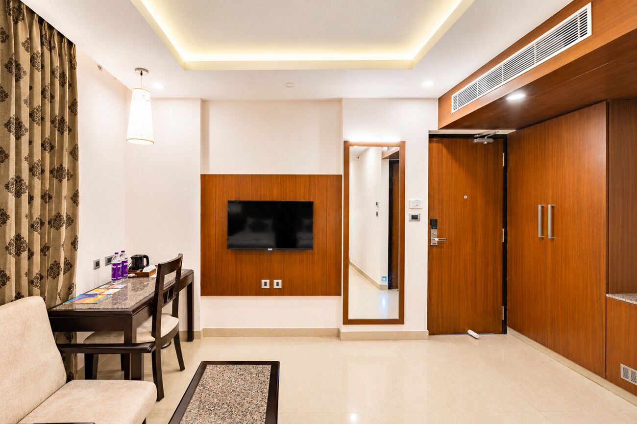 A modern living room with a flat-screen TV, wooden wardrobe, and a dining area with a table and chairs.