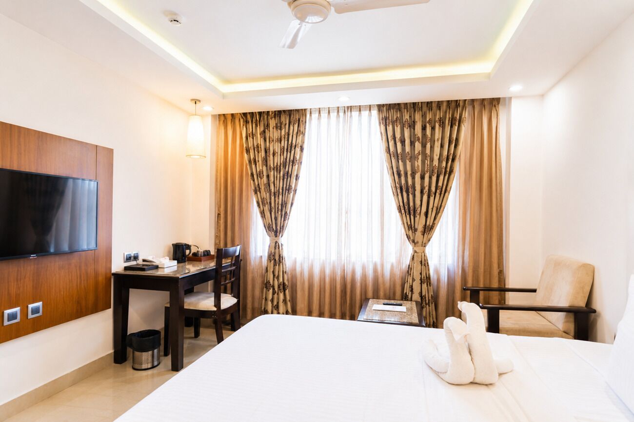 A hotel room with a bed, a desk, a chair, a television, and curtains.