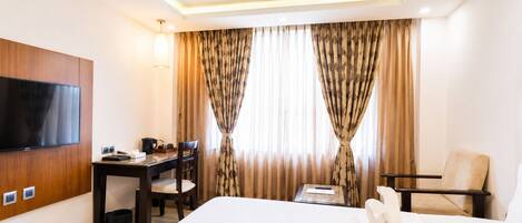 A hotel room with a bed, a desk, a chair, a television, and curtains.