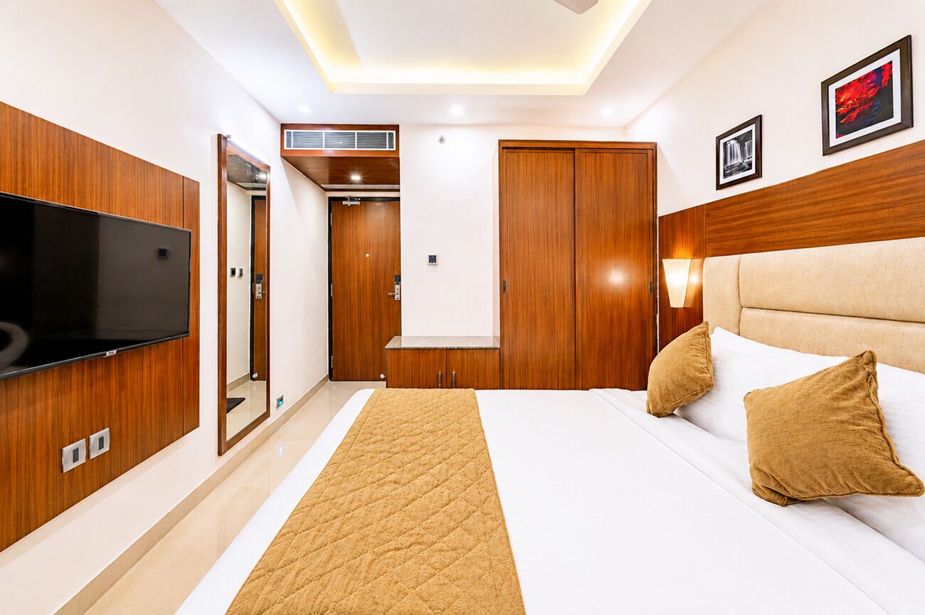 Habitación de hotel con cama, televisión, armario de madera y espejo.