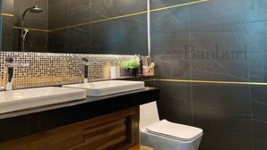 Ein Badezimmer mit dunkel marmorierten Wänden, einer schwarzen Arbeitsplatte, zwei Waschbecken, einem Spiegel und einer Toilette.
