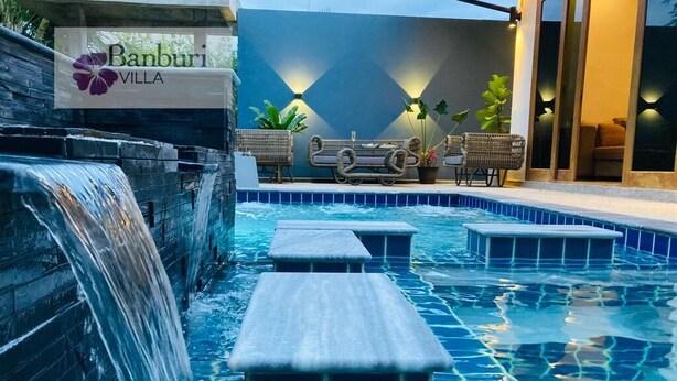 Ein Poolbereich mit Wasserfall, Liegestühlen und einem Schild für Banburi Villa.