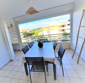 A dining area with a table and chairs, a hanging light fixture, and a view of buildings and greenery through large windows.