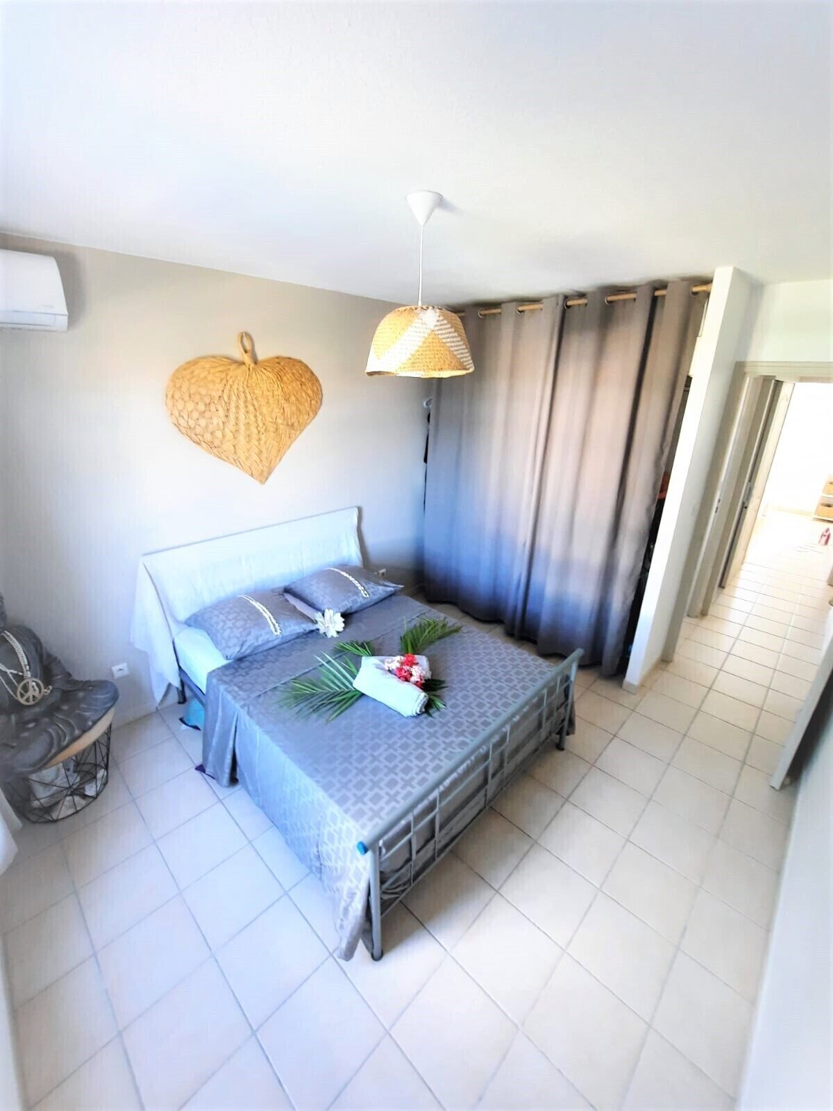 A neatly arranged bedroom with a bed, a chair, a hanging light fixture, and a wall-mounted heart-shaped decoration.