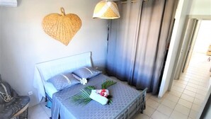 Een keurig opgemaakte slaapkamer met een bed, een stoel, een hanglamp en een hartvormige decoratie aan de muur.