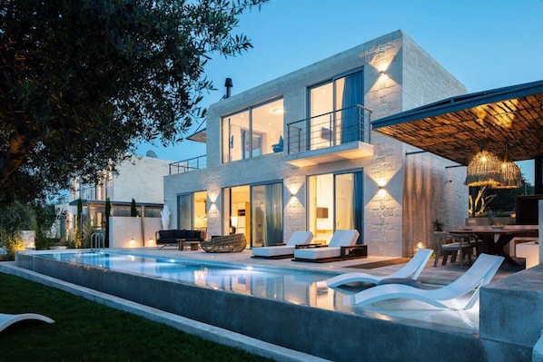 A modern two-story house with a swimming pool, outdoor seating, and a dining area.