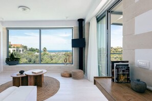 A modern living room with a large window, a flat-screen TV, and a cozy seating area.