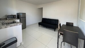 Een compact woongedeelte met een kitchenette, een zwarte bank en een eettafel.