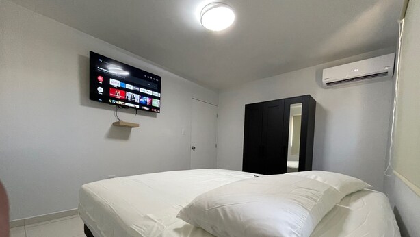 Een slaapkamer met een bed, een aan de muur bevestigde televisie en een airconditioning.