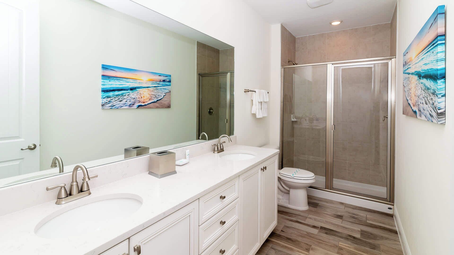 A modern bathroom with a double sink vanity, a toilet, and a glass-enclosed shower.