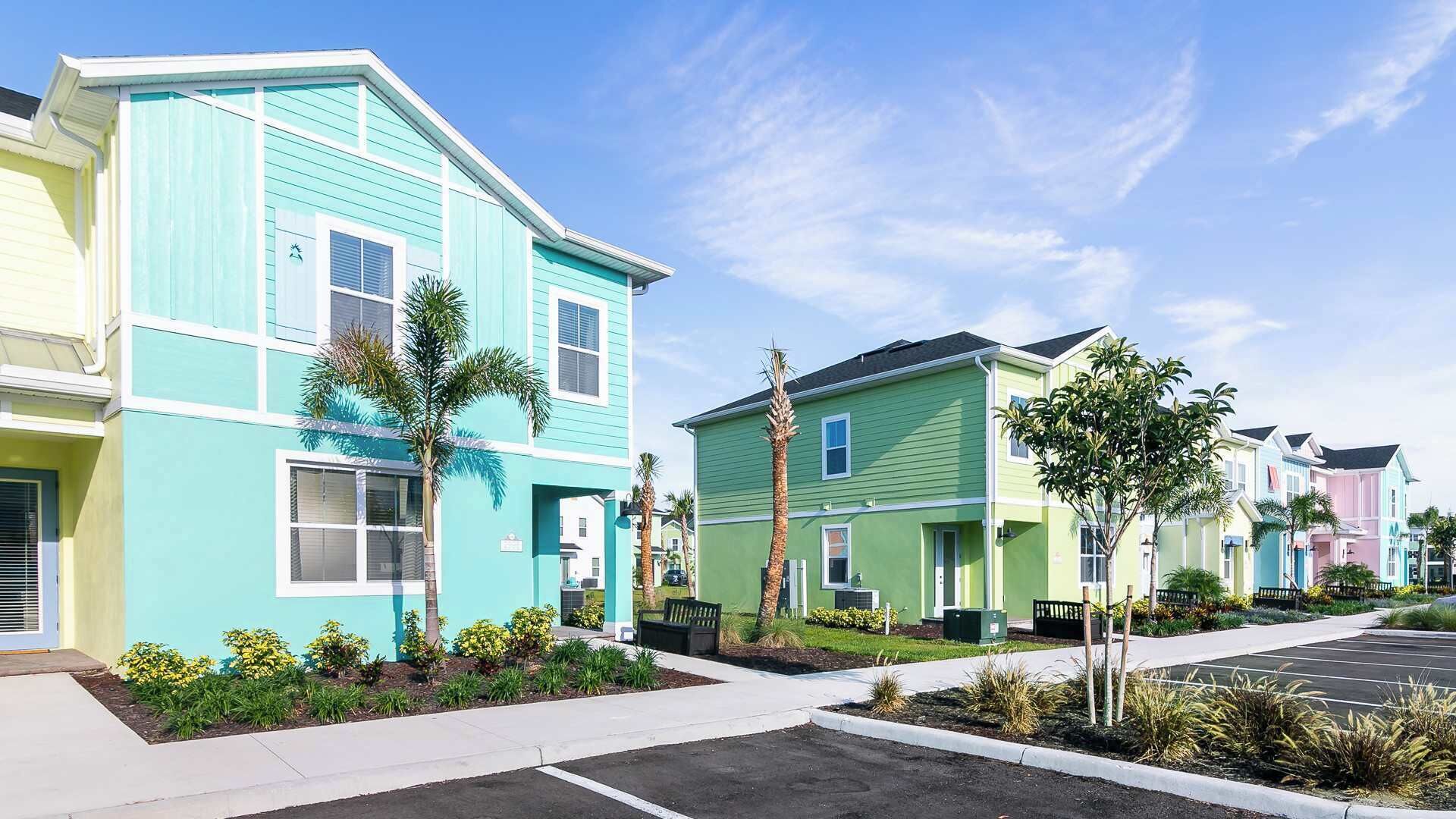 Une rangée de maisons de ville aux couleurs vives, avec une allée pavée et de petits espaces paysagers aménagés.