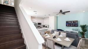Een moderne keuken met witte kastjes, een eethoek met een tafel voor vier personen en een plafondventilator.