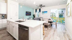 Een moderne keuken met een groot eiland, witte kasten en een vaatwasser. Er is een eetgedeelte met een tafel en stoelen, en een uitzicht op de achtertuin door een glazen deur.