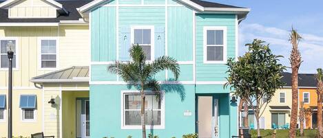 A two-story building with a light blue facade, a flat roof, and a small front porch with a bench.