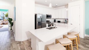 Een moderne keuken met witte kasten, roestvrijstalen apparatuur en een centraal keukenblok met barstoelen.