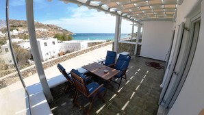 Un balcone con tavolo e sedie, affacciato su una zona costiera con edifici e cielo sereno.