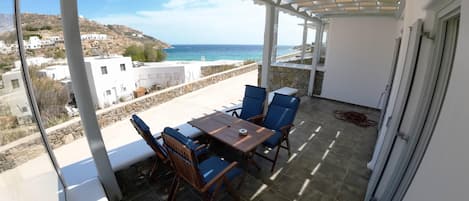 Un balcon avec une table et des chaises, donnant sur une zone côtière avec des bâtiments et un ciel dégagé.
