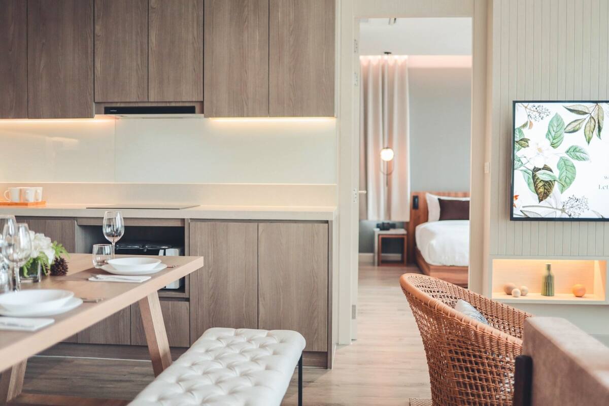 A modern kitchen with wooden cabinets, a dining table set for two, and a wicker chair.
