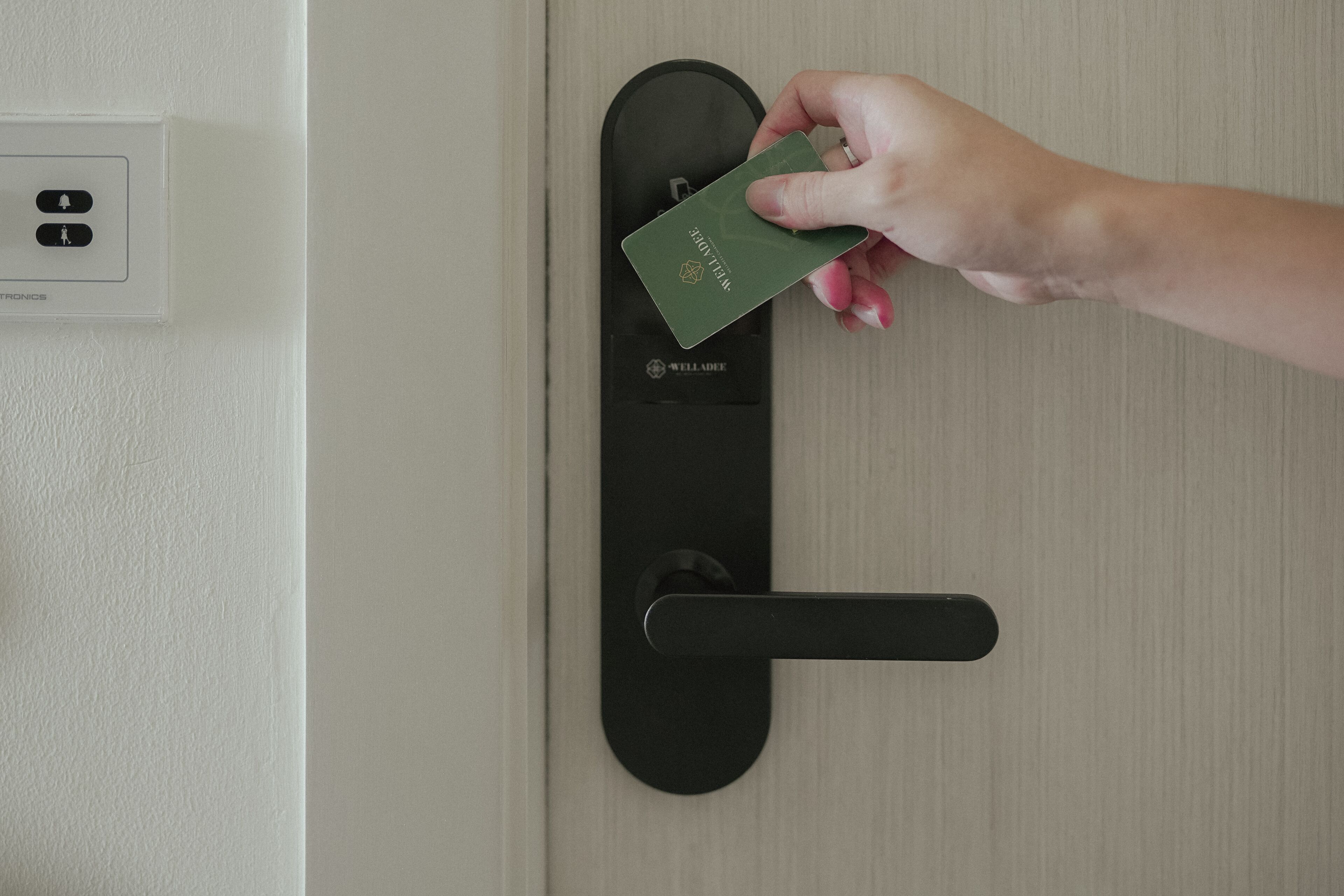 A hand holding a green card near a black card reader on a door.