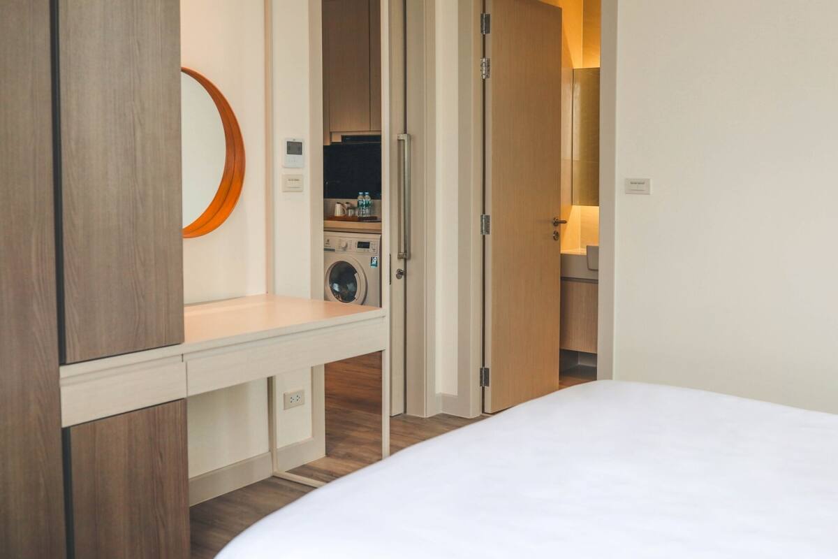 A hotel room with a bed, a washing machine, a mirror, and a small kitchenette.
