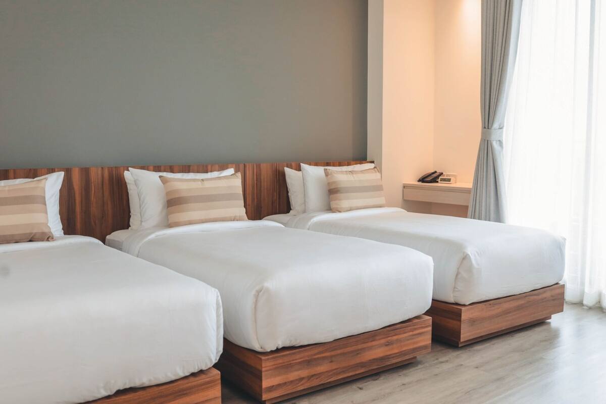 A hotel room with three beds, wooden headboards, and a bedside table with a phone.