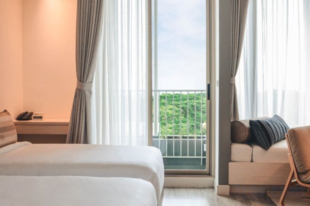 A hotel room with a bed, a sofa, a balcony with a view, and a telephone on a nightstand.