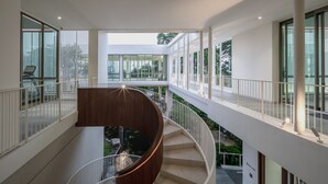 A modern interior with a curved staircase, glass railings, and a view of an outdoor area with greenery. - Welladee Wellness Chiang Mai (Chiang Mai)