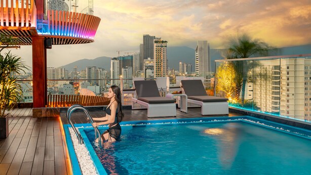 A rooftop pool area with a view of a city skyline, including high-rise buildings and mountains in the background. - MERCY EMERALD HOTEL (Da Nang)